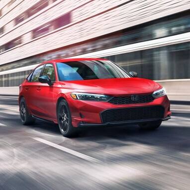 2027 Honda Civic Sedan Sport in Rallye Red front three-quarter view driving on a city street (Compact Sedan)